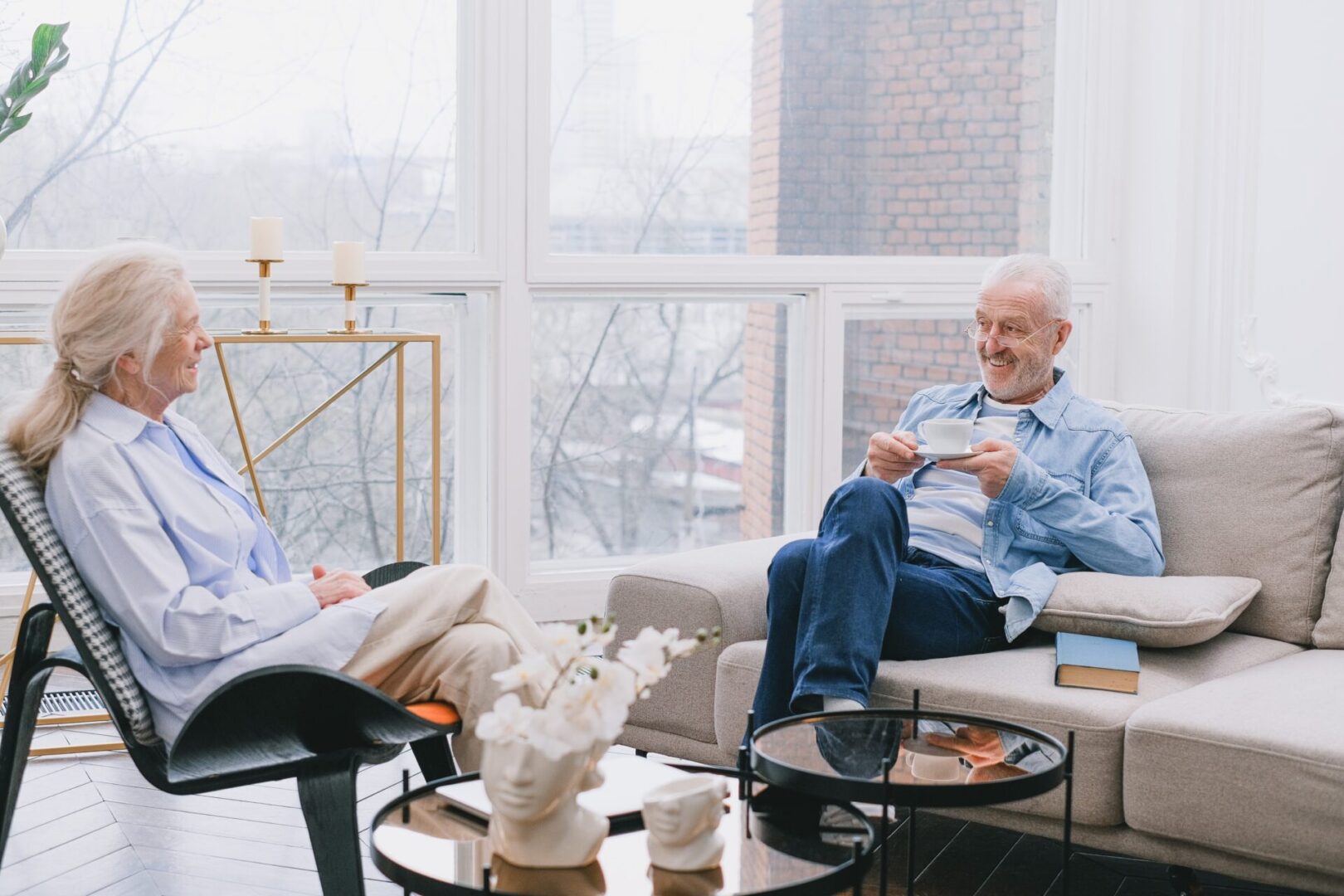 Two people sitting on a couch in front of a window.